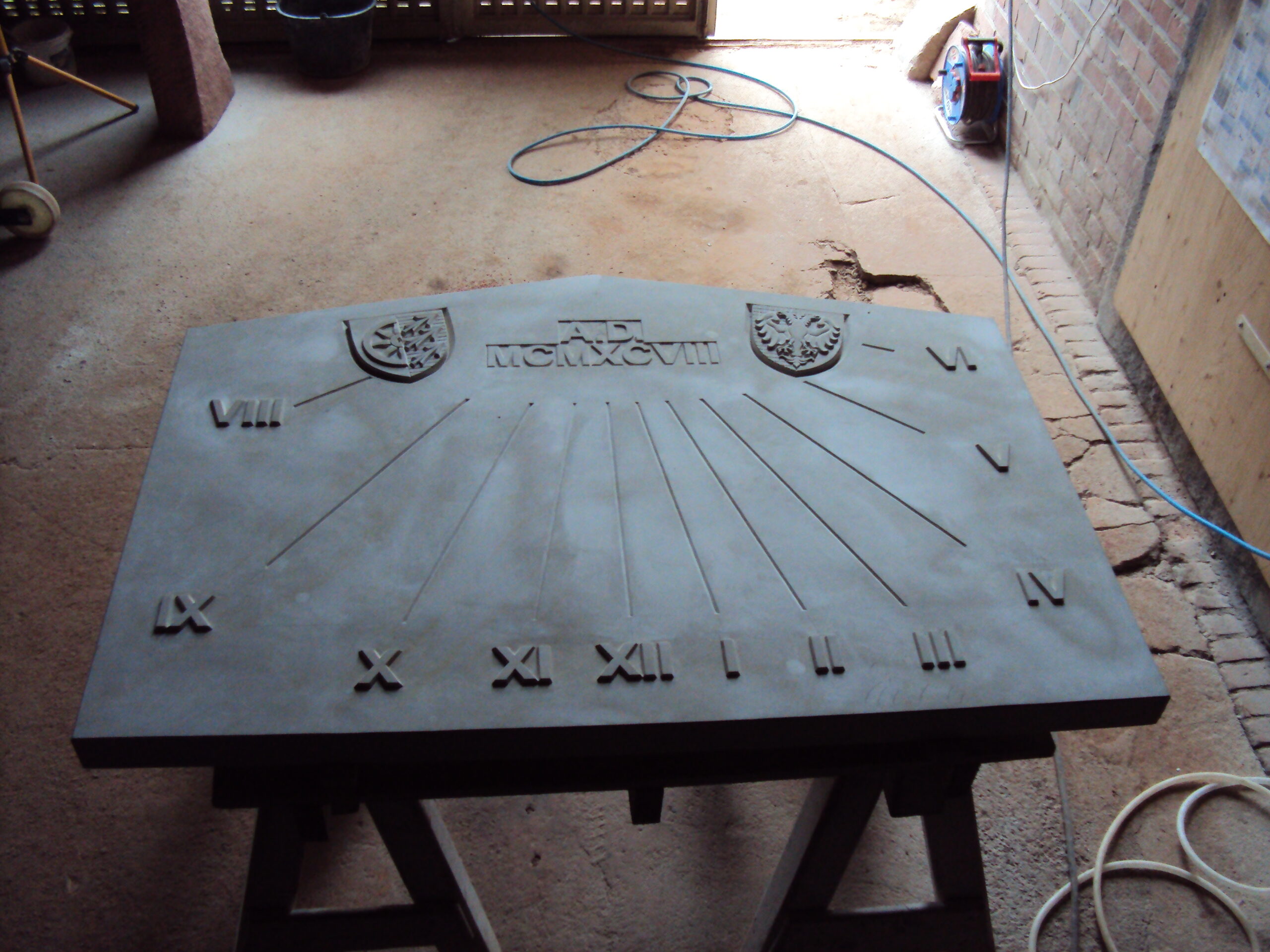 Große steinerne Sonnenuhr mit römischen Ziffern und Wappenreliefs.