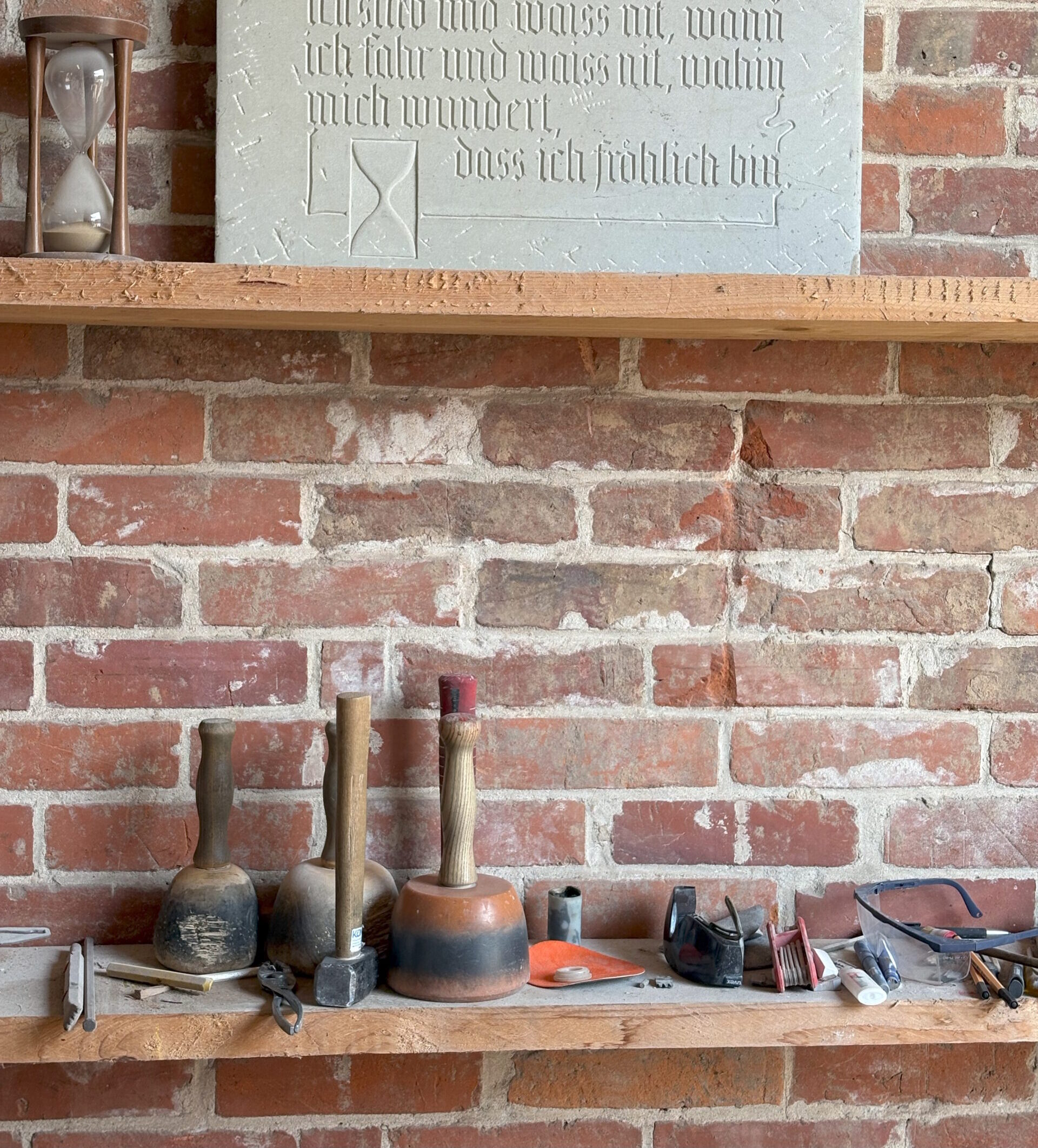 Werkstattregal mit Steinmetzwerkzeugen vor einer Ziegelwand.